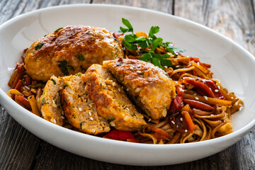 Asian style stir fried vegetables, pork meatballs and chow mein noodles on wooden table
