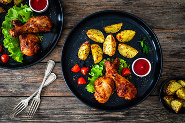 Oven baked chicken drumsticks with baked potato and fresh vegetables on wooden table
