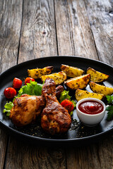 Oven baked chicken drumsticks with baked potato and fresh vegetables on wooden table
