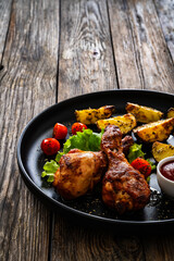 Oven baked chicken drumsticks with baked potato and fresh vegetables on wooden table
