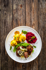 Baked pork cheeks with boiled potatoes and beetroots on wooden table
