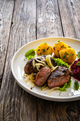 Baked pork cheeks with boiled potatoes and beetroots on wooden table

