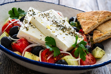 Greek style salad - fresh vegetables with feta cheese nad pita bread on wooden table
