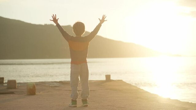 Boy jumping on the pier on the seashore against the backdrop of sunset