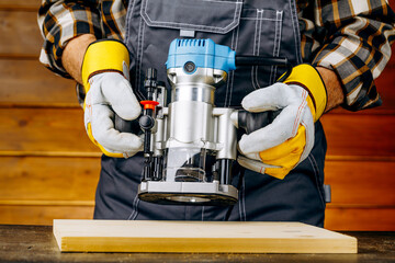 closeup of carpenter with hand wood router machine at work. closeup of routing a bevel into plank of pine woodworking construction tool concept furniture making diy.