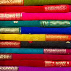 Closeup view of stacked saris or sarees in display of retail shop, for use as indian textiles background.