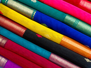 Closeup view of stacked saris or sarees in display of retail shop, for use as indian textiles background.