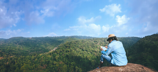 Asian man travel relax in the holiday. seats relax read books on rocky cliffs. On the Moutain summer. In Thailand - 759501265