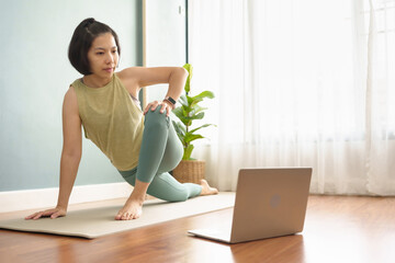 Healthy Young Asian Japanese sporty woman practicing yoga lesson on yoga mat in online class on...