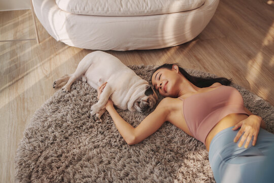 Relaxed Young asian Woman Enjoying a Restful Moment with Her pug Dog on a Shaggy Rug in Sunlit Living Room