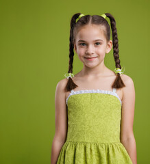 A young girl in green dress is smiling. She has her hair in pigtails