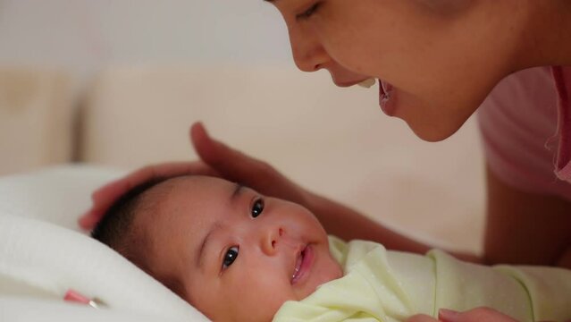 Close up of asian young mother playing with newborn baby smile in a nursery. Parent looking and kiss at infant. Talk, touch, Enhance child's development. Childhood, Maternity, Children, Motherhood.