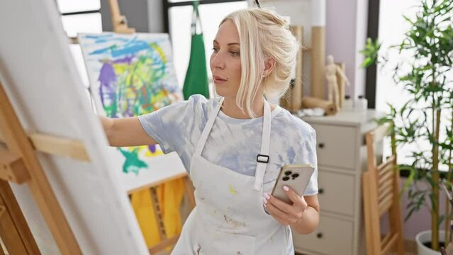 Engrossed in creativity, young, blonde woman artist concentrating on drawing via smartphone in art studio, embracing modern technology and traditional artistry.
