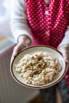 The hands of a senior home cook hold a plate with a national Slovak dish: Strapacky - Bryndzove Halusky