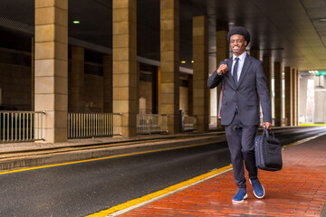 African architect holding computer bag and drawings tube walking in the city