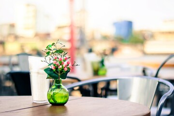 Flower in green vase with paper napkin on the table in open air restaurant.