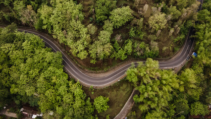 aerial view, asphalt road winding through forest and countryside.