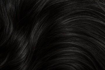 Fototapeta premium Brunette or black hair. Female long dark hair in black. Beautifully laid curls. Closeup texture in a dark key. Hairdressing, hair care and coloring. Shading gray hair. Background with copy space.