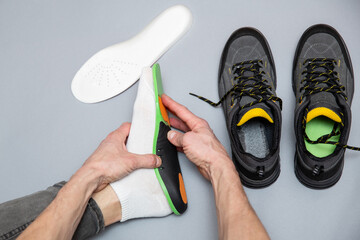 Close up of man hands fitting orthopedic insoles on a gray background. - 759564839