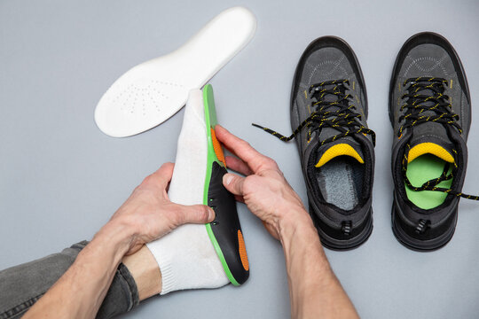 Close up of man hands fitting orthopedic insoles on a gray background.