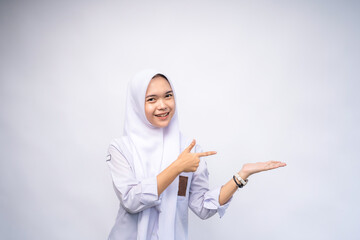 Excited Female Indonesian high school student in white and grey uniform, pointing at the copy space beside her, isolated by white background