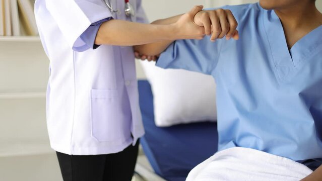 Female doctor doing physiotherapy and diagnosing male patient arm and shoulder pain in hospital examination room.