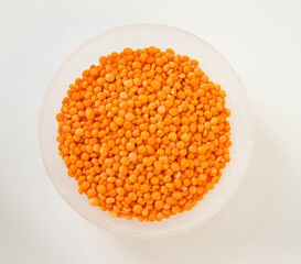 Raw organic red lentils in a round glass plate. White background. Top view.