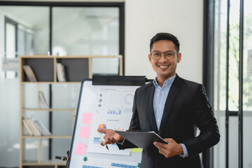 Asian businessman in a suit is standing in front of a white board with a presentation.