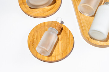 close up of face beauty serum dropper bottle of matte glass and bamboo lid on wooden tray on white background. Skin care package