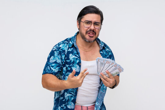 Dodgy and sleazy middle-aged man in a Hawaiian shirt pompously showing off a wad of cash, portraying wealth, standing isolated on a white background.