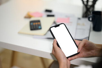 Unrecognizable businesswoman hands holding mobile phone with white screen sitting at desk