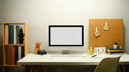 Creative workplace with blank computer monitor, camera, coffee cup and peg board on wall