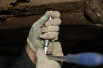 A mechanic in a hole under a car unscrews nuts in a garage while repairing a car. The mechanic unscrews the nuts removing the protection from the car to drain the old oil from the car.