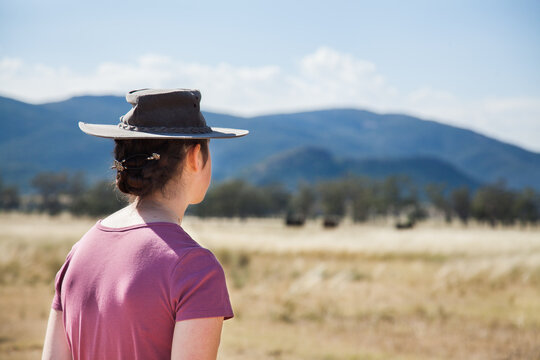 A teen farm kid in an akubra hat standing in farm paddock