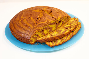 A slice of cake with a blue plate on a white background. The cake is cut in half and has a zigzag...