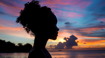 Silhouette of a woman with afro hairstyle at sunset. A dramatic sunset in gorgeous shades of pink, blue, yellow and grey. A dreamlike view.
