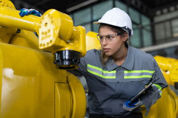 Female engineer checking and maintaining robot arms machine at factory. Technician woman in uniform...