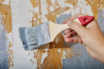 Close up of paintbrush in hand of house painter painting chipboard wall with gray paint.