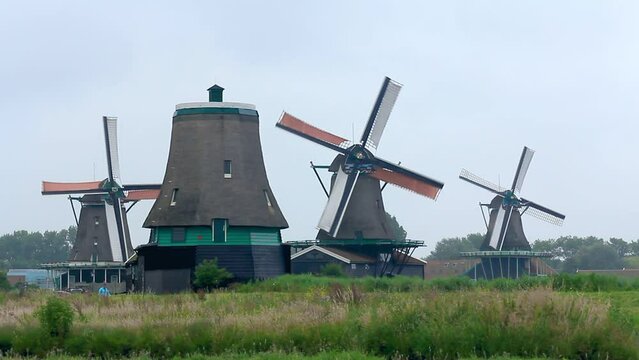 Paisaje holand&eacute;s de molinos de viento centenarios en funcionamiento con canales y gente caminando por camino circundante
