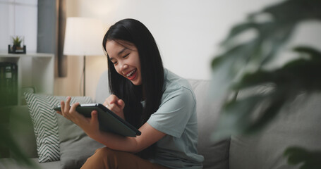 Selective focus, Happy young woman sitting on sofa using digital tablet for online shopping cashless in living room at home - 759606456