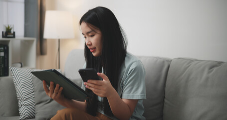 Selective focus, Happy young woman sitting on sofa using digital tablet and mobile phone for online shopping in living room at home - 759606483