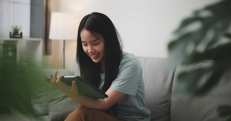 Selective focus, Happy young woman sitting on sofa using digital tablet for online shopping cashless in living room at home - 759606484