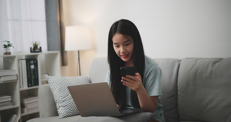 Selective focus ,Happy young woman sitting on sofa using laptop and mobile phone for online shopping in living room at home - 759606614