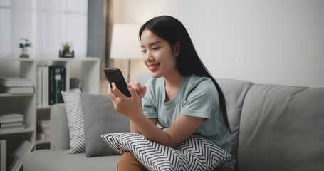 Happy young woman sitting on sofa enjoy using mobile phone for online shopping cashless in living room at home, Technology money wallet and Online payment concept