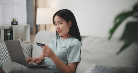 Selective focus, Young asian woman sitting on sofa holding credit card making online payment for...