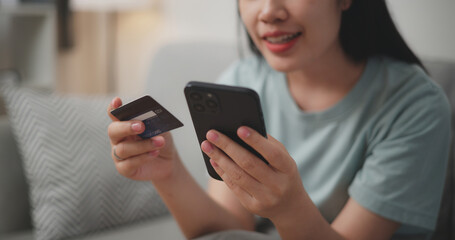 Fototapeta premium Selective focus, Hands of Young asian woman sitting on sofa holding credit card making online payment for purchase in web store using smartphone.