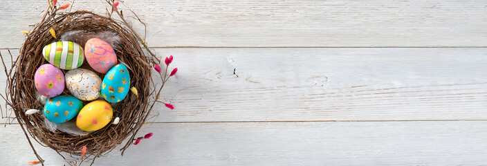 Colorful Easter Eggs in Bird Nest on white wooden background: Festive Spring Decoration.  Copy space for banner.