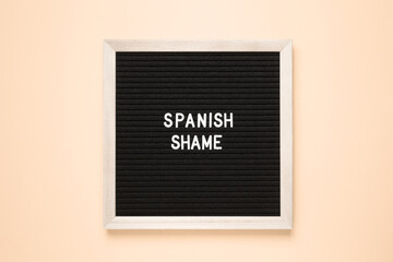 The word spanish shame on black letter board over isolated beige background. Psychological concept