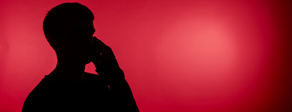 dark silhouette of a male student talking with a smartphone on a pink background, close-up with free space for text - Powered by Adobe