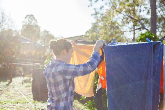 Young woman pegging clothes to washing line in backyard